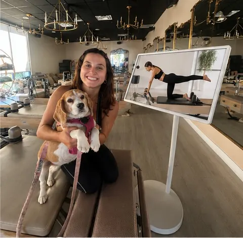 An instructor with her beagle on a reformer beside the on-demand class screen