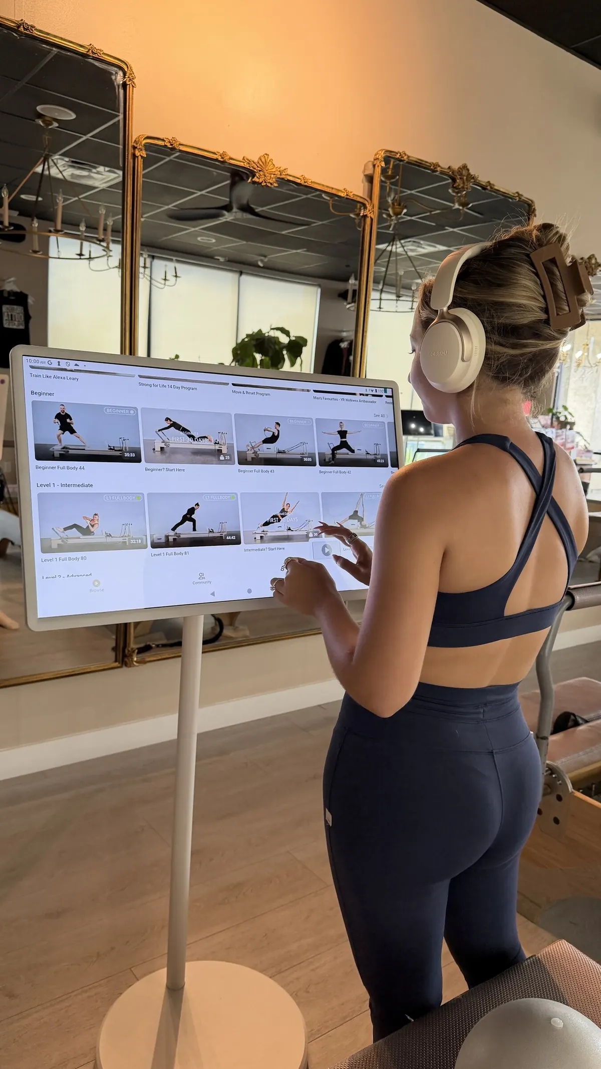 A client in headphones choosing a workout on the studio screen beside her reformer