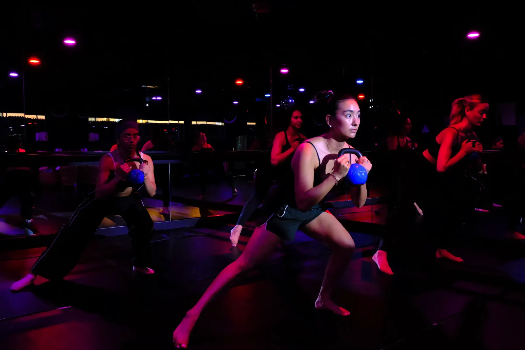 A hot room class lunging with kettlebells under coloured light